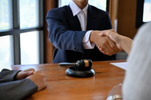 A well-dressed male attorney shakes hands with a satisfied client, officially hired to handle their legal case after a successful agreement.