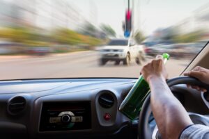 Blurry accident scene on road seen through windshield, depicting man drinking and driving.