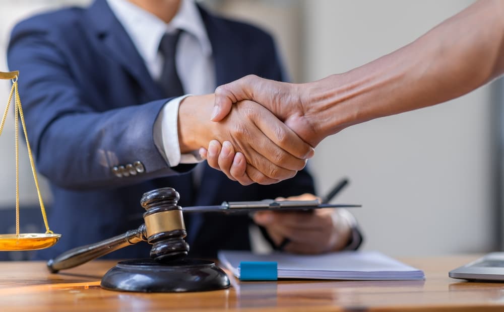 Close-up of male lawyer shaking hand with client in courtroom, working on wooden table - Legal law and justice concept.