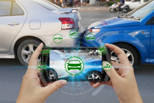 Hands holding a smartphone capturing rear-end car accident scene with virtual icons for damage assessment