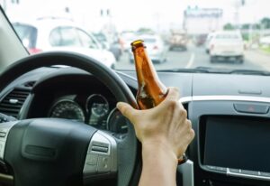 A driver holding a bottle of alcohol while driving, illustrating the concept of drunk driving. 