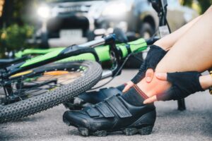 Cropped shot of a female cyclist suffering from ankle pain after a car accident on the road. Concept of a car crash involving a bicycle on the road.