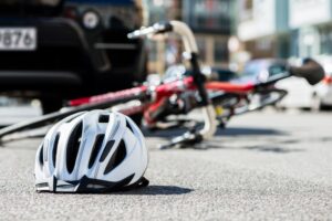 Close-up of a bicycling helmet fallen on the asphalt next to a bicycle after car accident on the street in the city