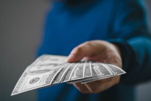 A close-up image of a hand offering multiple U.S. dollar bills