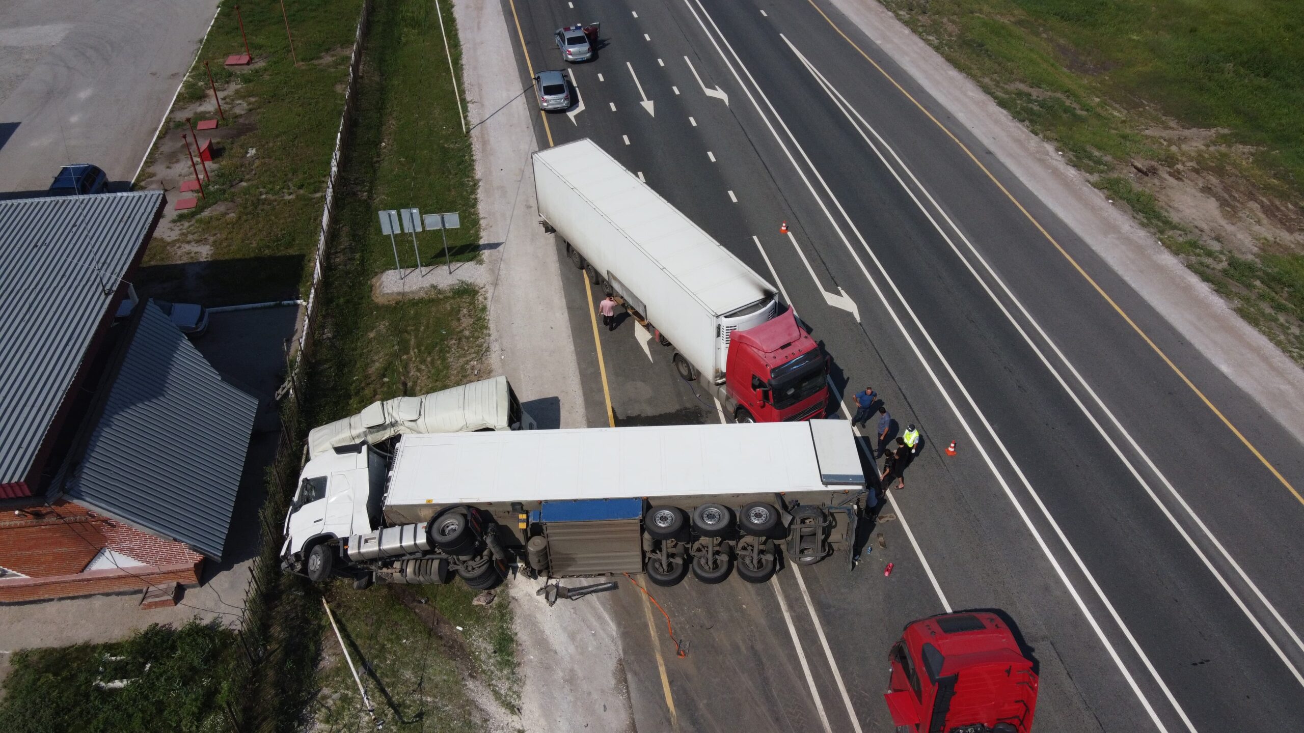 Aerial view of a car accident involving a truck and a bus. The truck and bus are visibly damaged, with debris scattered around the scene. Emergency vehicles are present, and the road is blocked. The surrounding area includes trees and buildings, captured from a drone's perspective.