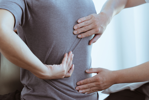 A close-up of hands pressing on a person's mid-back, suggesting back pain or muscle tension.