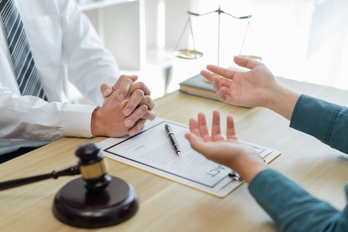 A lawyer and a client discussing a contract at a desk, with a gavel and scales of justice visible in the foreground.