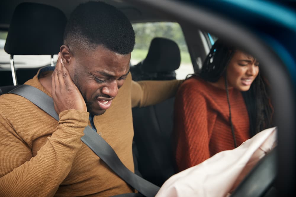 Passenger injuries after Colorado car accident—understanding your legal rights. Injured passengers holding their neck and arm after a Colorado car accident inside a vehicle with deployed airbag.
