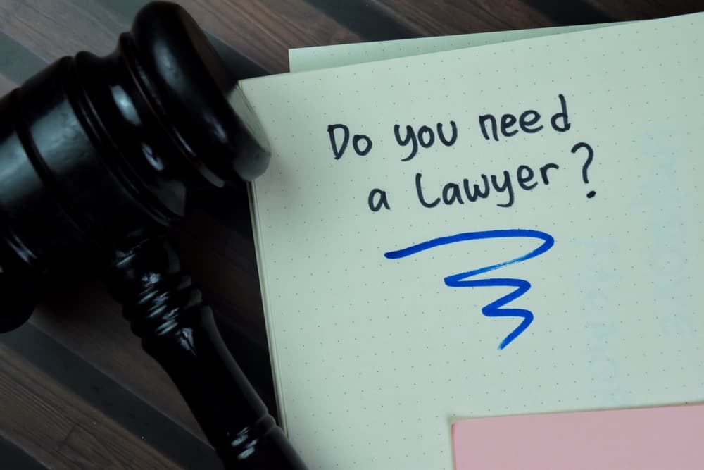 Gavel beside a notebook with handwritten words “Do you need a lawyer?” representing the decision to hire legal help after filing an insurance claim.